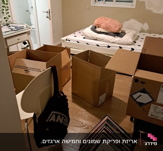 חדר עם קופסאות קרטון פתוחות וערימת תקליטים